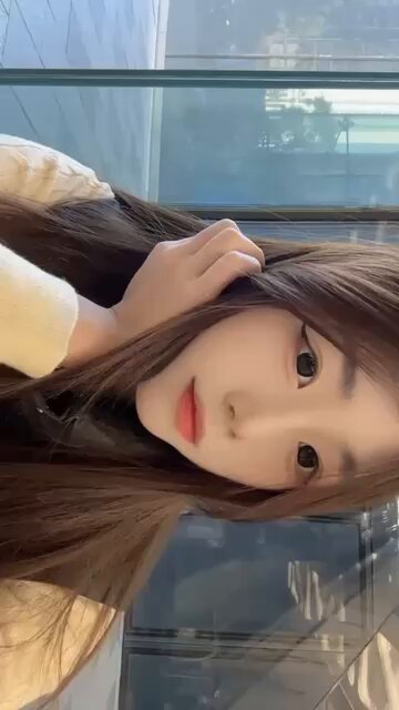 ガラスカーテンウォールの前に立つ長髪の美女が頬を撫でて誘惑する、超セクシー！