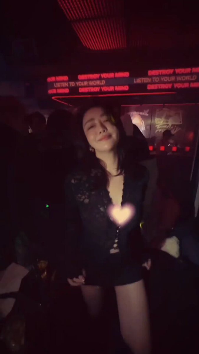 Nightclub babe in black stockings and a mini skirt seductively shakes her hips — a mesmerizing smile under heart-shaped lights