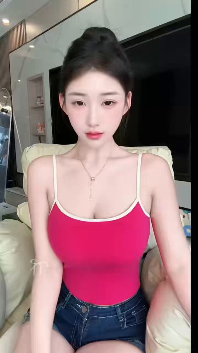 清純な大きな瞳の美女、ピンクのキャミソールで爆乳を見せつける誘惑ショー。超ショートパンツでヒップを強調し、ソファで色っぽく誘う！